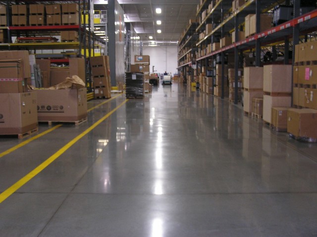 A polished concrete floor runs between two rows of shelves in a Volkswagen parts warehouse in WI. Boxes are stacked high on both sides of the aisle.